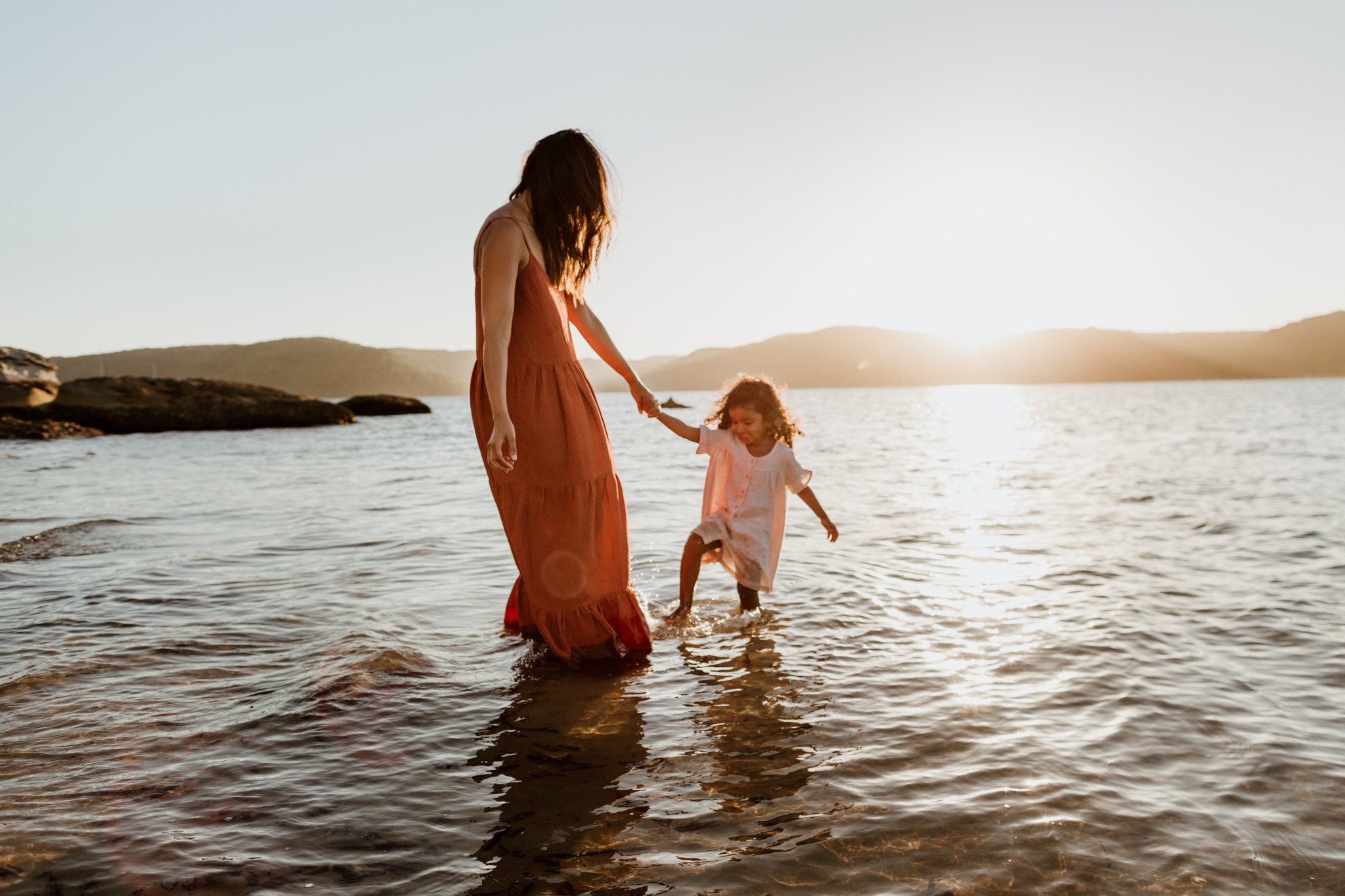 Mother & daughter playing in a body of water with the sun gleaming in the background