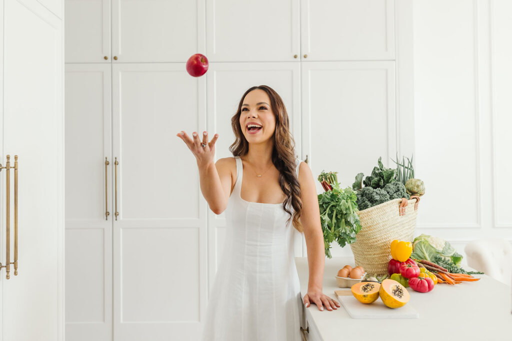 Nutrition coach playfully tossing an apple, surrounded by fresh produce.
