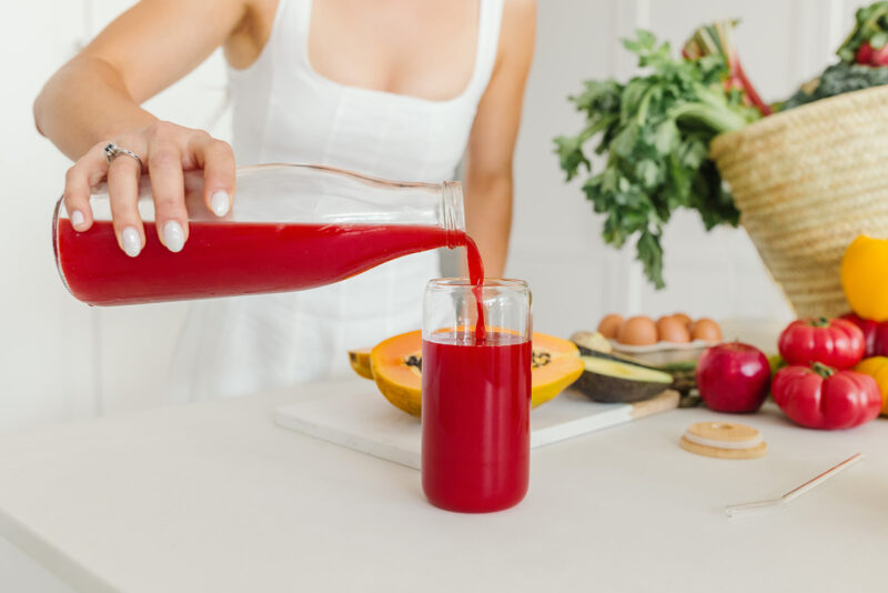 Nutrition coach pouring red juice amidst a setting of fresh produce.